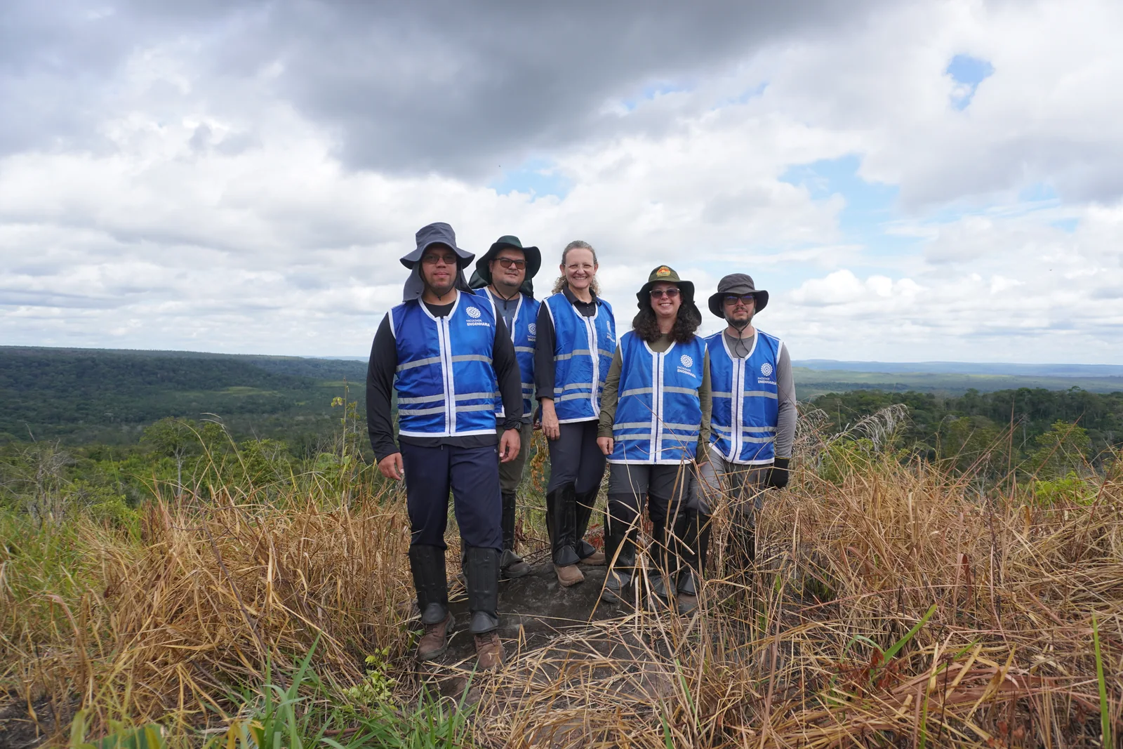 Cinco integrantes da equipe com coletes azuis em uma paisagem de campo